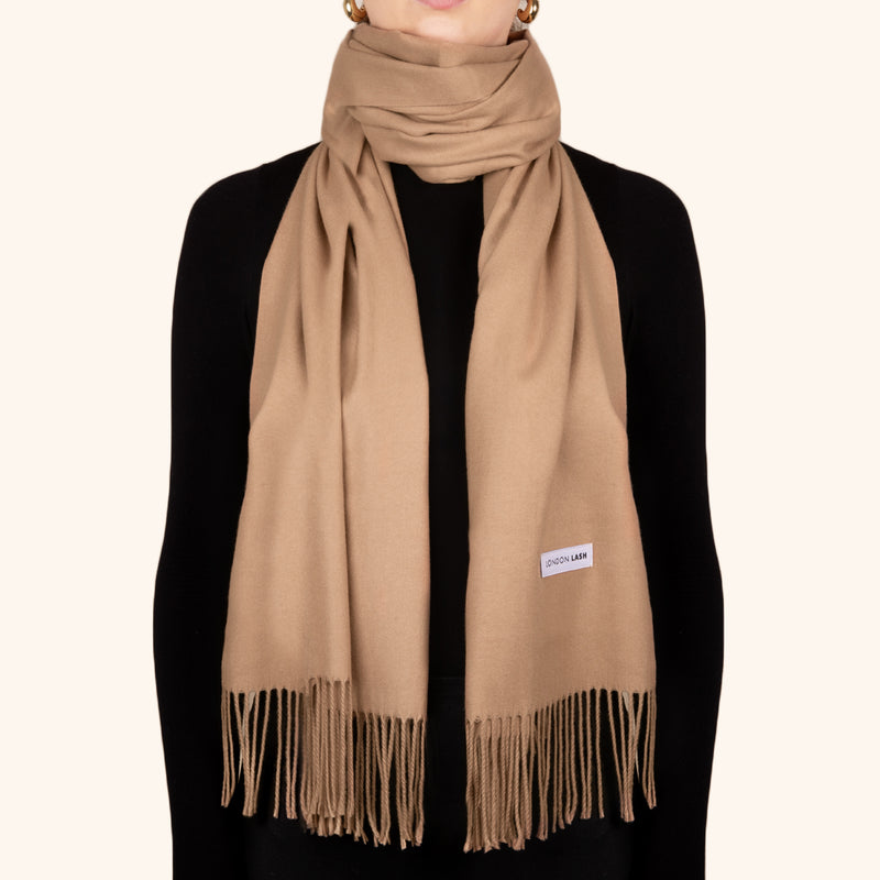A person wearing a beige oversized wool scarf with fringes, wrapped around the neck and tied at the waist.